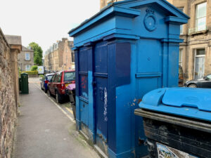 View of police box from pavement, including adjacent wheelie bin and parked cars
